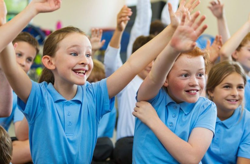 Islington primary school pupils raising their hands in an engaging classroom supported by a JobsinED SEN Teaching Assistant